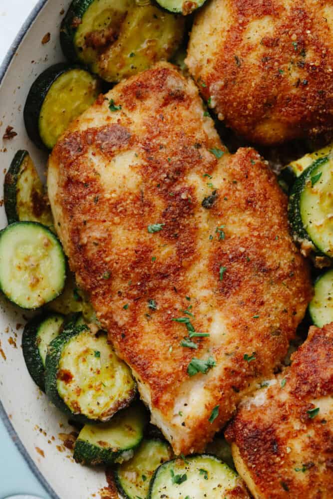 Crispy parmesan garlic chicken with zucchini is a fantastic one-pan meal that the family will love. Crispy chicken is breaded with an amazing parmesan garlic crust paired with tender zucchini sautéed to perfection! Close-up of crispy parmesan garlic chicken and zucchini.
