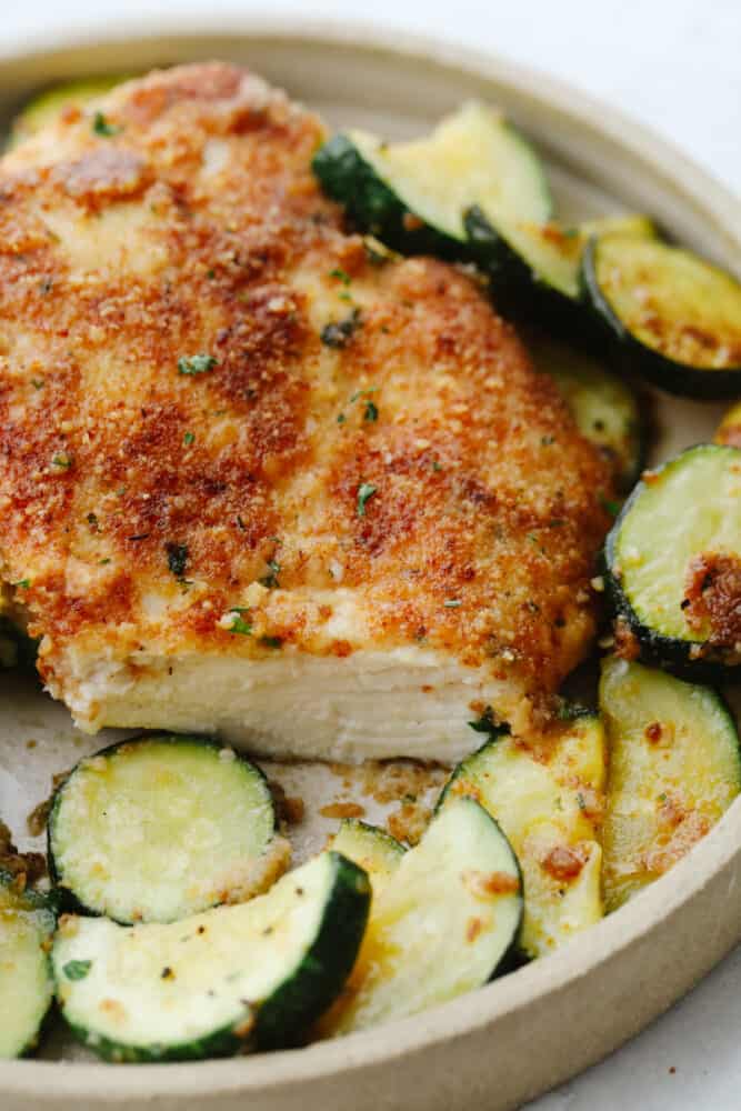 Crispy parmesan garlic chicken with zucchini is a fantastic one-pan meal that the family will love. Crispy chicken is breaded with an amazing parmesan garlic crust paired with tender zucchini sautéed to perfection! Slice cut out of parmesan garlic chicken with zucchini.