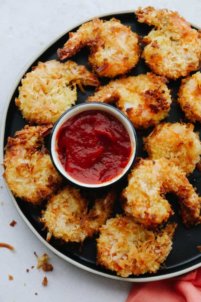 Coconut shrimp are insanely delicious! One of the best appetizers out there, these mouthwatering air fried coconut shrimp are crispy, lightweight and completely delightful! This appetizer is one that is sure to have your guests coming back for more! Air fried shrimp on a platter with some dipping sauce.