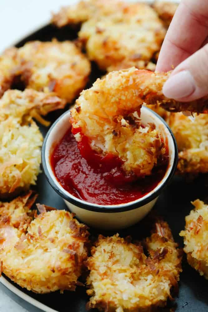 Coconut shrimp are insanely delicious! One of the best appetizers out there, these mouthwatering air fried coconut shrimp are crispy, lightweight and completely delightful! This appetizer is one that is sure to have your guests coming back for more! Air fried shrimp being dipped into sauce.