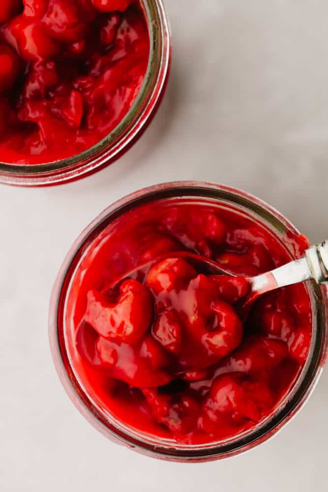 This cherry pie filling comes together so quickly and will make enough for you to have on hand for pies all year!! Delectable and sweet with a hint of tartness, this filling is perfection and you won't be able to go back to store-bought ever again!! Cherry pie filling in a jar with a spoon.