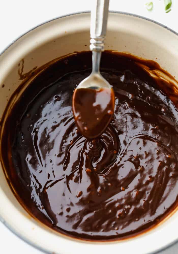 Rich, sweet, and salty, hoisin sauce is the perfect foundation for all of your Asian-inspired dishes. This homemade variation packs so much delicious flavor, you won't want store-bought again! Hoisin sauce in a pot, being scooped up with a spoon.