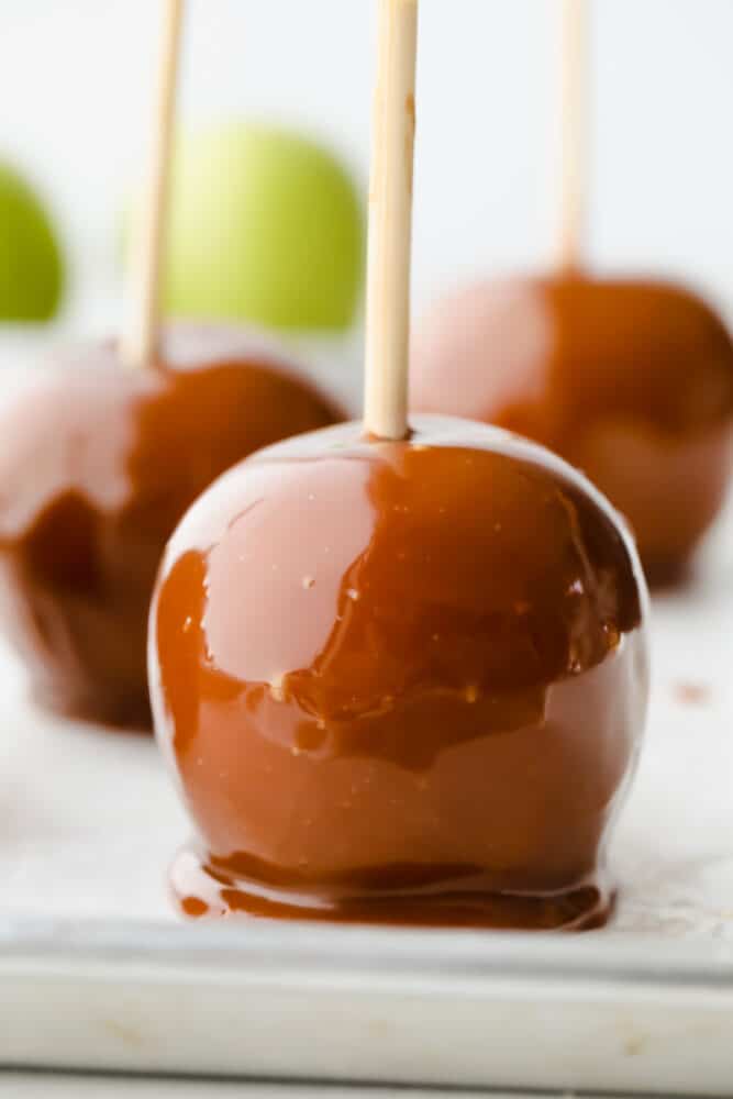 Celebrate fall by making these gourmet homemade caramel apples! They are the perfect blend of tart and sweet, topped with layers of indulgent caramel. 3 caramel apples on parchment paper.