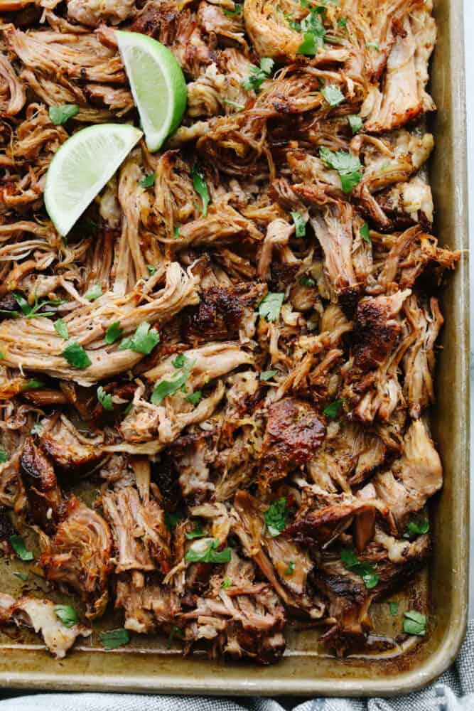 Slow cooker pork carnitas are an amazingly easy and delicious recipe that is full of flavor and cooks all day to tender and juicy perfection! This is definitely a carnitas recipe that you will make again and again! Shredded pork in a pan with a lime.
