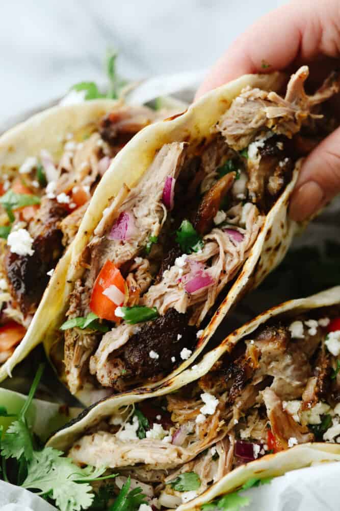 Slow cooker pork carnitas are an amazingly easy and delicious recipe that is full of flavor and cooks all day to tender and juicy perfection! This is definitely a carnitas recipe that you will make again and again! Pork carnitas in a tortilla with toppings.