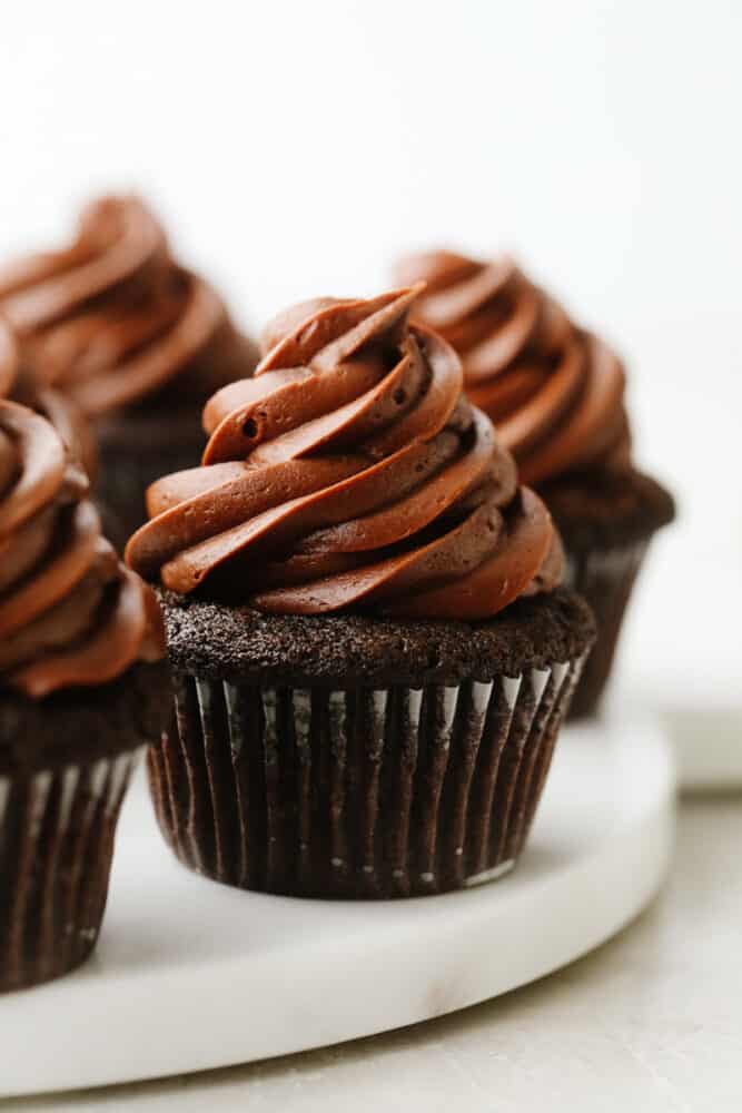 For treats that are incredibly moist, fudgy, and delicious, this is your go-to recipe! Topped with smooth chocolate buttercream, these chocolate cupcakes are a classic dessert your friends and family will go crazy over. Frosted chocolate cupcakes on a serving dish.