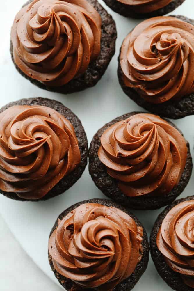 For treats that are incredibly moist, fudgy, and delicious, this is your go-to recipe! Topped with smooth chocolate buttercream, these chocolate cupcakes are a classic dessert your friends and family will go crazy over. Top-down shot of frosted chocolate cupcakes.