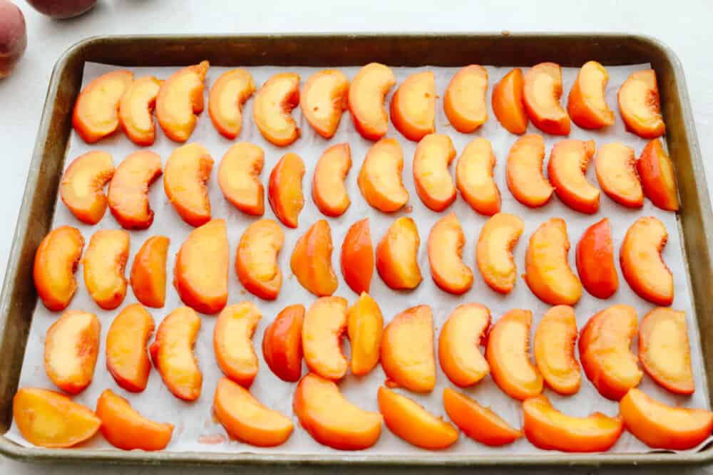 Freezing peaches is the best because they can be used in EVERYTHING! If you want to enjoy delicious peaches all year round then look no further because, with this recipe, you can have juicy, delicious peaches whenever you want! Peaches lined up on parchment paper on a baking sheet.