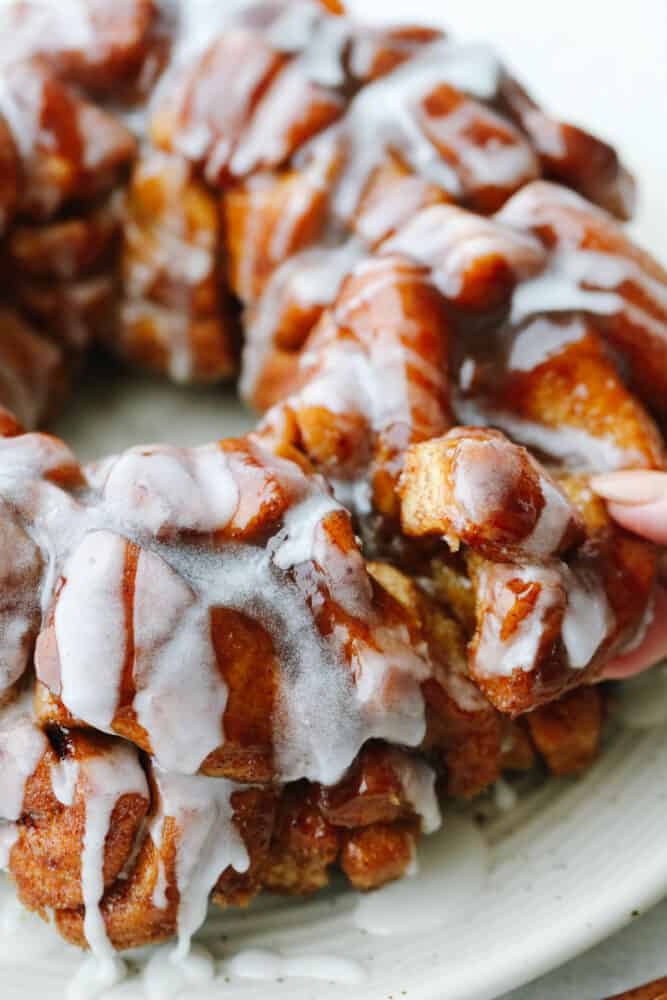 Cinnamon roll monkey bread is the easiest pull-apart dessert! It is amazingly soft, warm, and layered in decadent icing. Closeup of taking a piece of cinnamon roll monkey bread.