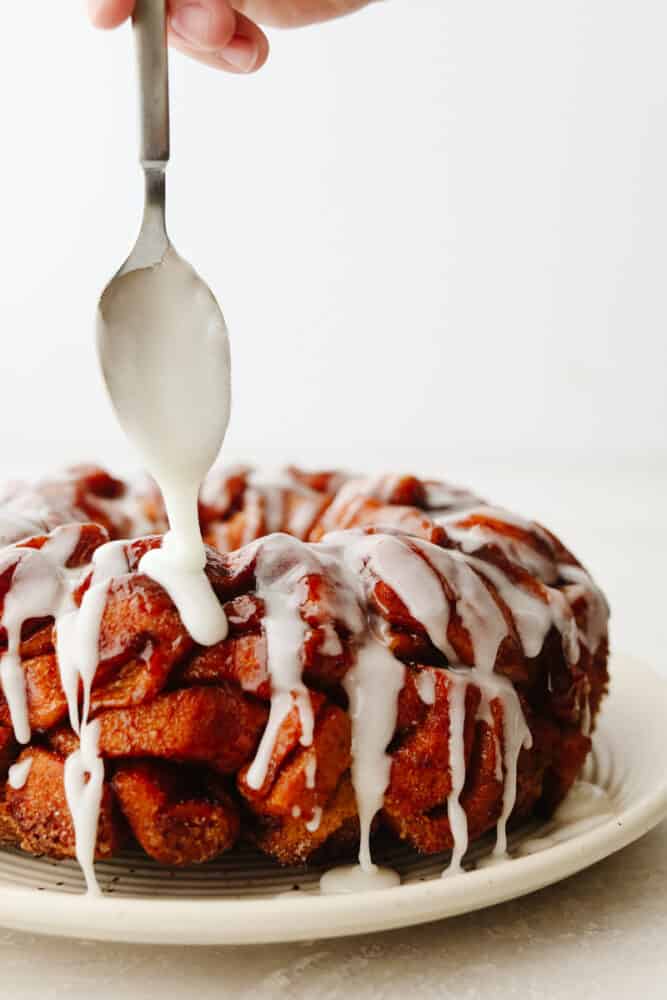 Cinnamon roll monkey bread is the easiest pull-apart dessert! It is amazingly soft, warm, and layered in decadent icing. Drizzling icing on cinnamon roll monkey bread.
