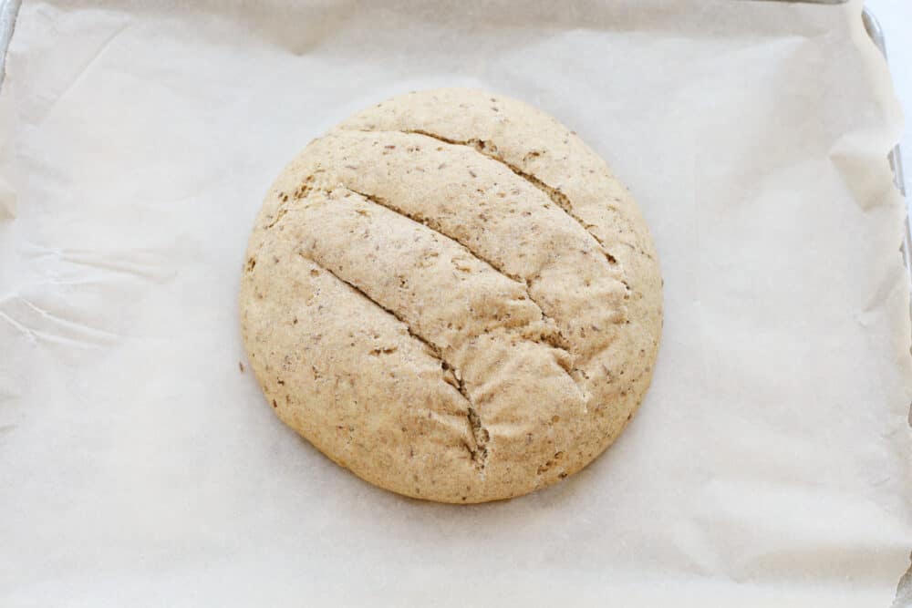 Rye Bread is a soft light loaf of heavenly flavor and a crust that's to die for! Super easy and wholesome, you and your loved ones are going to love this homemade bread! Formed round loaf of rye bread with cuts on a lined cookie sheet.