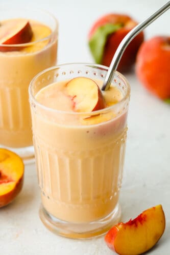 This peach smoothie is juicy and refreshing and provides a burst of delicious flavor! The texture is just perfect, the color is beautiful and the taste is something everyone in your family will go crazy for! Smoothie with a peach and a straw.