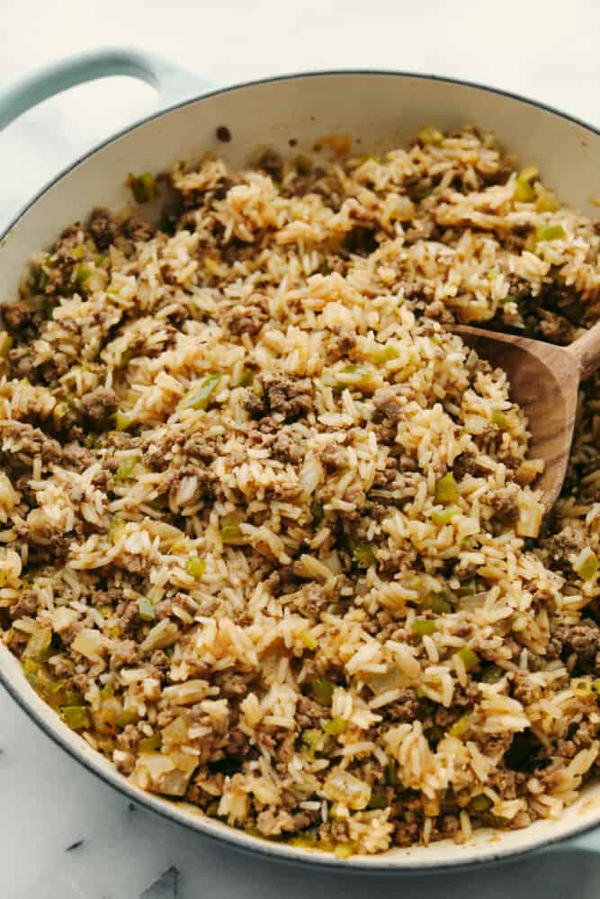 Dirty rice is packed with Cajun flavor and the texture is to die for! It has the most amazing blend of delicious spices, meats, and rice that will definitely be something that your family will go crazy for! Rice with meat and veggies being served with a wooden spoon.