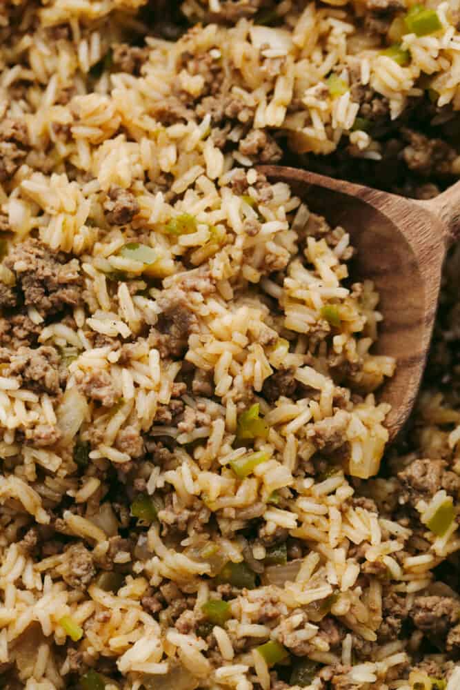Dirty rice is packed with Cajun flavor and the texture is to die for! It has the most amazing blend of delicious spices, meats, and rice that will definitely be something that your family will go crazy for! Dirty rice being served with a wooden spoon.