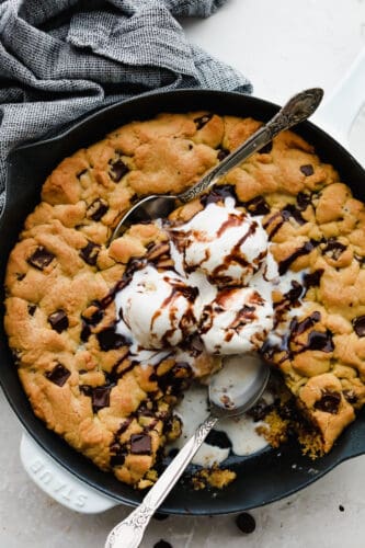 This ooey-gooey skillet cookie brings homemade cookies to the next level! It is warm, sweet and the chocolate just melts right in your mouth! You definitely won't be able to stop at just one bite! A chololate chip skillet cookie with ice cream on top being eaten with a spoon.