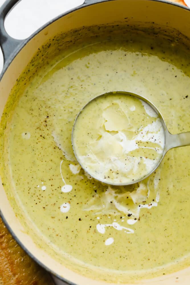 This zucchini soup has an amazing savory flavor, fresh vegetables, and is topped with the perfect drizzle of cream. Healthy and hearty, each spoonful will have you hooked with its silky-smooth goodness! Scooping creamy zucchini soup with a ladle.