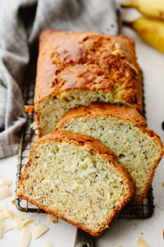 Coconut banana bread is sweet and insanely delicious! The moist texture combined with its amazing taste will make it hard to stop after just one slice! Sliced coconut banana bread on a cooling rack.