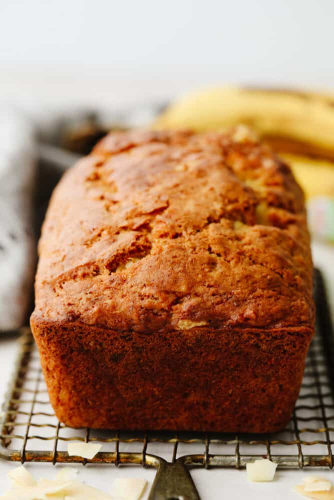 Coconut banana bread is sweet and insanely delicious! The moist texture combined with its amazing taste will make it hard to stop after just one slice! A loaf of bread on a cooling rack.