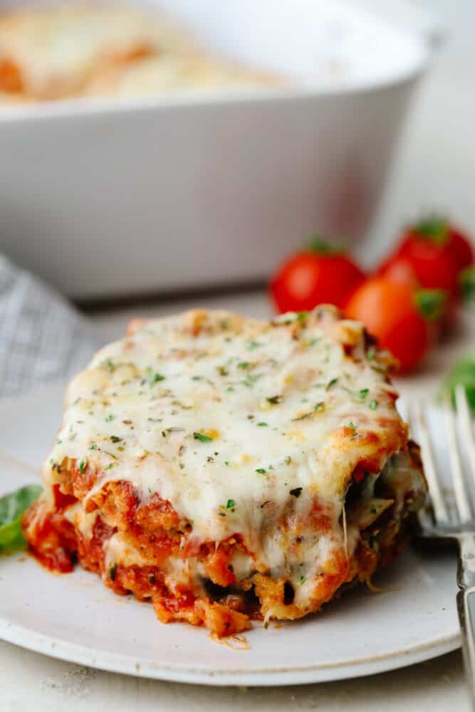 Eggplant parmesan is a tangy, crispy, cheesy masterpiece! Delicious eggplant covered in a delightful mix of herbs and spices, this recipe will knock your socks off! A slice of eggplant parmesan on a plate.