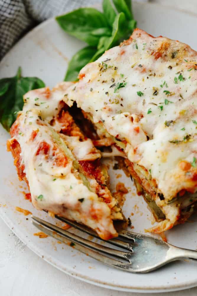 Eggplant parmesan is a tangy, crispy, cheesy masterpiece! Delicious eggplant covered in a delightful mix of herbs and spices, this recipe will knock your socks off! Eggplant parmesan being cut into with a fork.