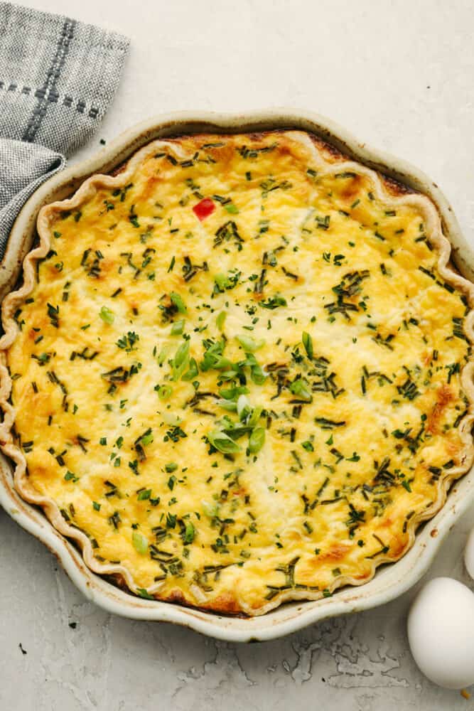 Creamy and custard-like, the best quiche starts with a basic recipe and has endless options for adding meat, vegetables, and herbs. This delicious staple recipe is perfect for breakfast, lunch, or dinner. A full quiche in a pie tin.