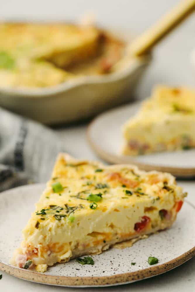 Creamy and custard-like, the best quiche starts with a basic recipe and has endless options for adding meat, vegetables, and herbs. This delicious staple recipe is perfect for breakfast, lunch, or dinner. A quiche slice on a stoneware dish.