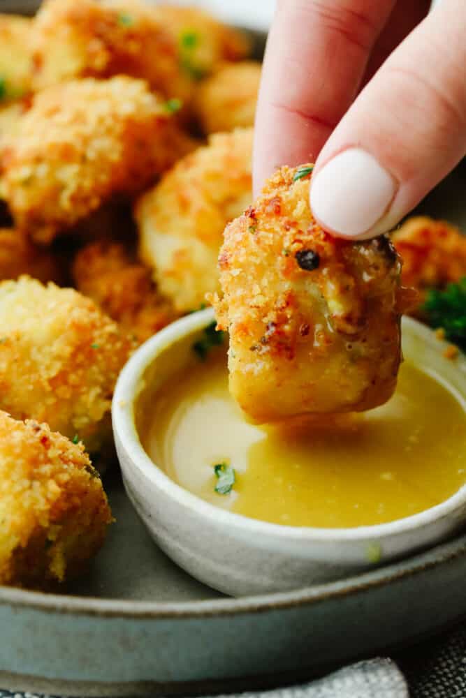 Air fryer chicken nuggets are absolute perfection! They are crispy on the outside, tender on the inside, and are just waiting to be dipped in any of your favorite sauces! Your family will go crazy over them! An air fried chicken nugget being dipped into honey mustard sauce.