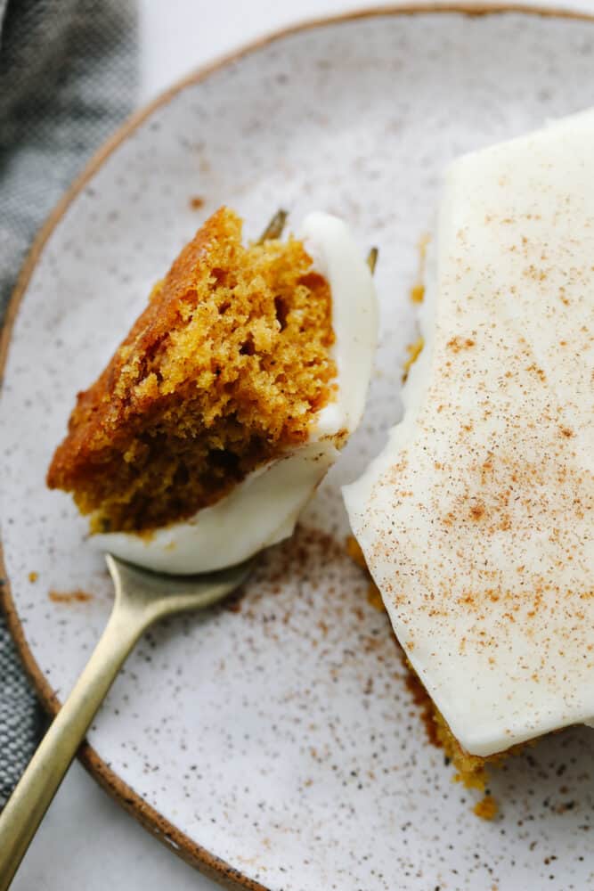 Pumpkin spice sheet cake not only tastes amazing but it feeds a crowd! Top it with some tangy cream cheese frosting and you have yourself a dessert to remember! A fork cutting into a slice of pumpkin spice cake.