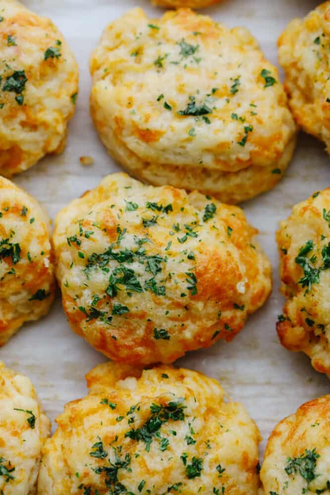 These delicious copycat Red Lobster cheddar biscuits are better than the real thing! Warm, buttery, and ready in 20 minutes! Closeup of cheddar biscuits on parchment paper.