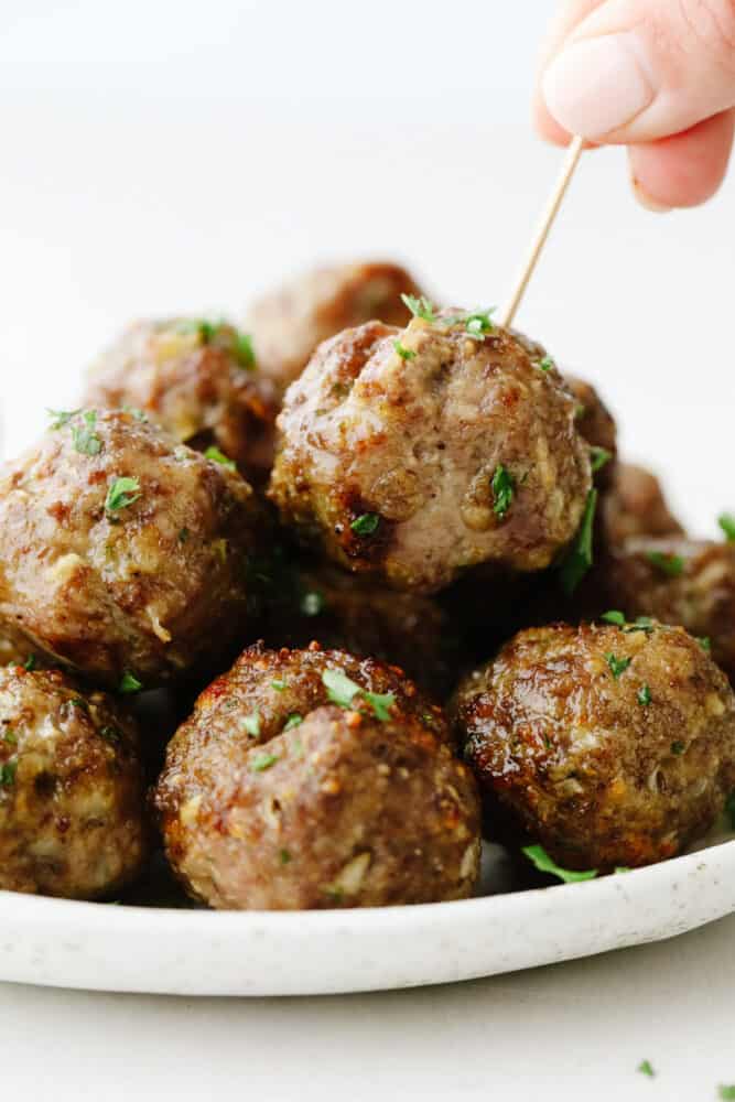 Air fryer meatballs are tender, juicy, and delicious! They are SOO good and this will be a recipe that your family will want you to make again and again! A stack of meatballs with someone putting a toothpick in one of them.