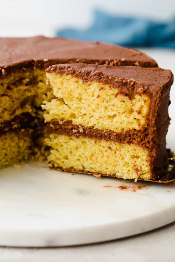 Yellow cake is a classic dish that we all know and love! Perfectly moist with a light and fluffy texture, it's a cake that we make ALL the time because everyone loves it! Yellow cake with chocolate frosting with a slice being pulled out.