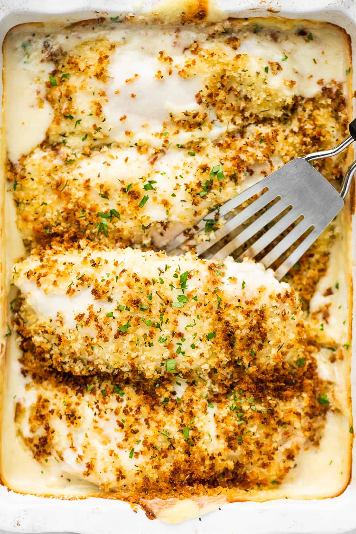 Creamy Swiss Chicken Bake is absolutely delicious. Chicken breasts are smothered in an easy-to-make Swiss cheese sauce, covered in crispy, seasoned breadcrumbs, then baked until bubbly. It's an easy chicken casserole the whole family will love! A spatula lifting a piece of creamy Swiss chicken out of a casserole dish.
