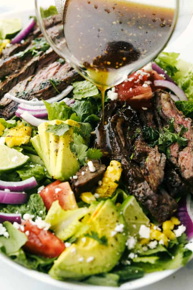 Juicy skirt steak, fresh veggies, and feta cheese- all tossed in a delicious tangy glaze. Steak salad with honey balsamic dressing is a mouthwatering meal infused with bold, savory flavor! Pouring honey balsamic glaze over salad.