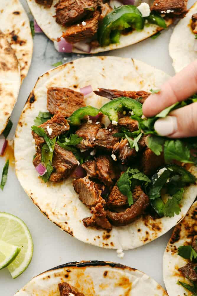 Beef brisket tacos are full of delicious flavor and topped with perfectly tender and juicy meat. This is a meal that your entire family will go crazy over! Beef brisket on a tortilla with someone putting on toppings.
