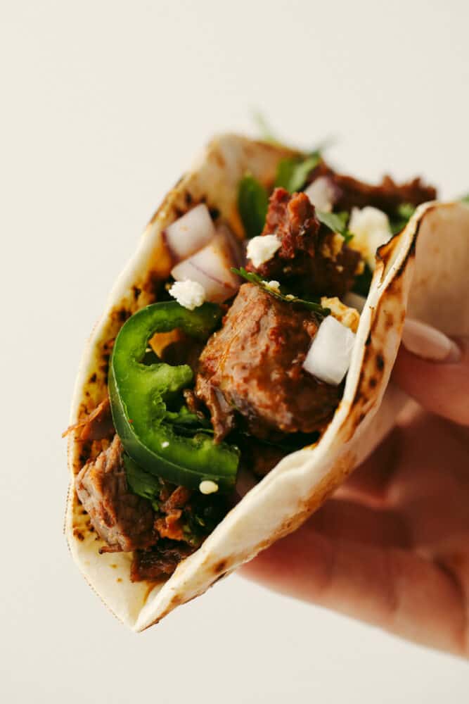 Beef brisket tacos are full of delicious flavor and topped with perfectly tender and juicy meat. This is a meal that your entire family will go crazy over! A close up of a beef brisket taco folded in half being held in someone's hand.
