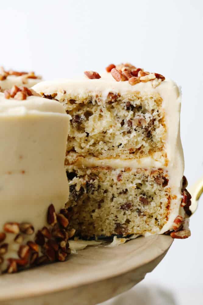 Soft, tender, and filled with nutty goodness, this butter pecan cake is perfect for fall! Browned butter cream cheese frosting and fresh chopped pecans make each bite a dream. Taking a slice of butter pecan cake.