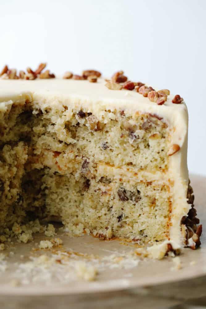 Soft, tender, and filled with nutty goodness, this butter pecan cake is perfect for fall! Browned butter cream cheese frosting and fresh chopped pecans make each bite a dream. A slice cut out of a full cake.