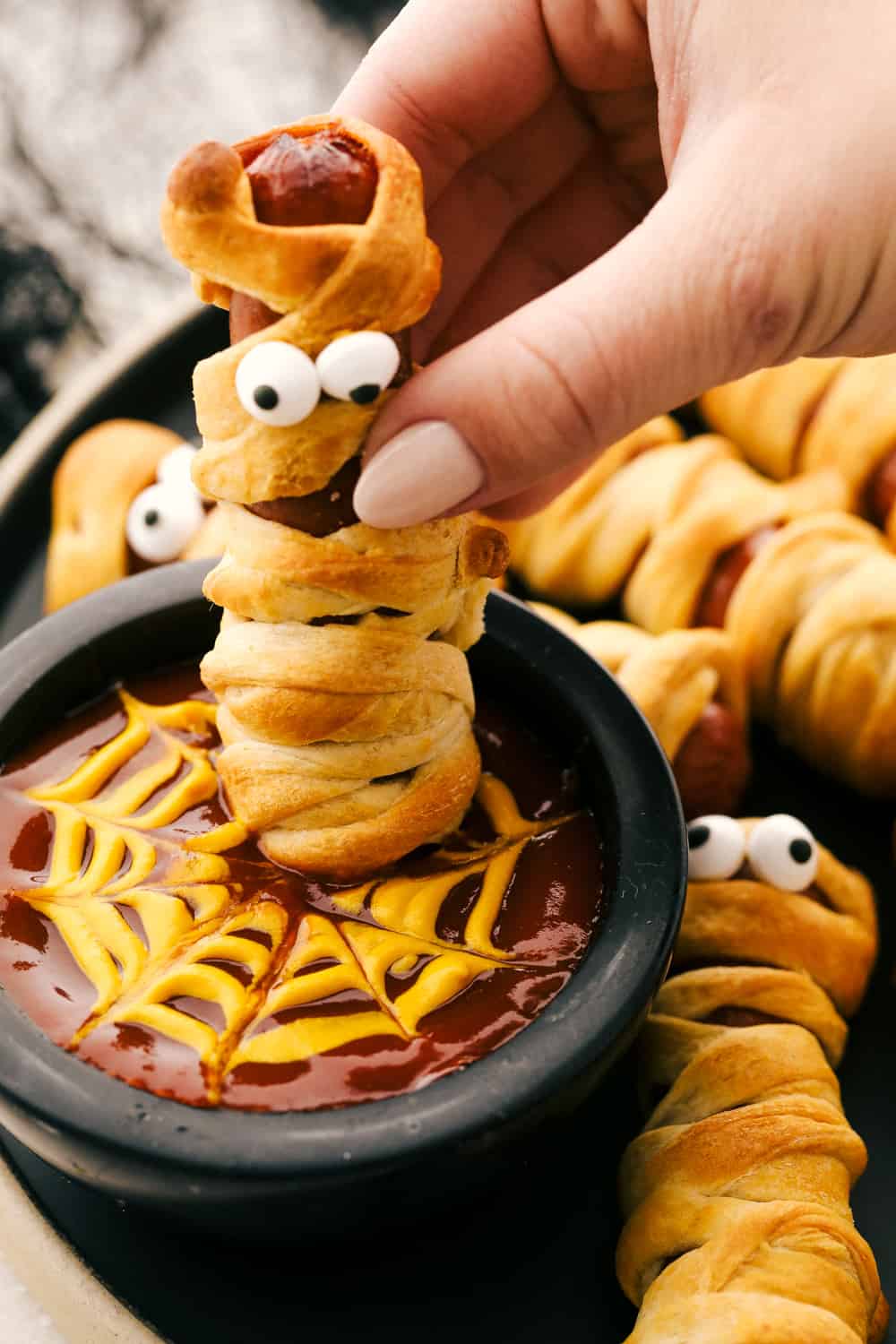Nothing screams fun, quite like Mummy Hot Dogs for Halloween dinner. Serve these fun little vittles before trick or treating or at your next Halloween party. Dipping a mummy dog into spider web sauce.