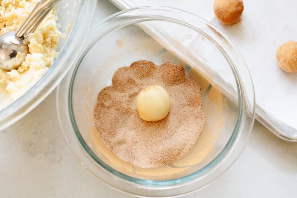 These snickerdoodle are delightfully soft and full of delicious cinnamon flavor! They are SOO GOOD and you won't be able to stop at just one! A snickerdoodle dough ball being rolled into cinnamon sugar.