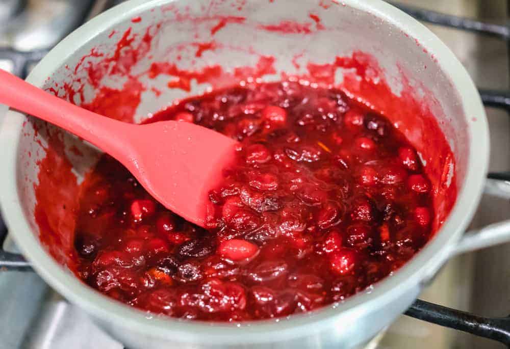 This cranberry sauce is the perfect mixture of sweet and tart! It's made with fresh cranberries and topped with orange zest to really set it apart! Cooking cranberries in a pan.
