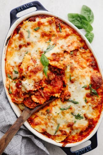 This baked ravioli is a knockout dinner that is sure to be loved by all! It's smothered in melty mozzarella, parmesan, and a tasty meat sauce! Baked ravioli in a casserole dish, garnished with basil.