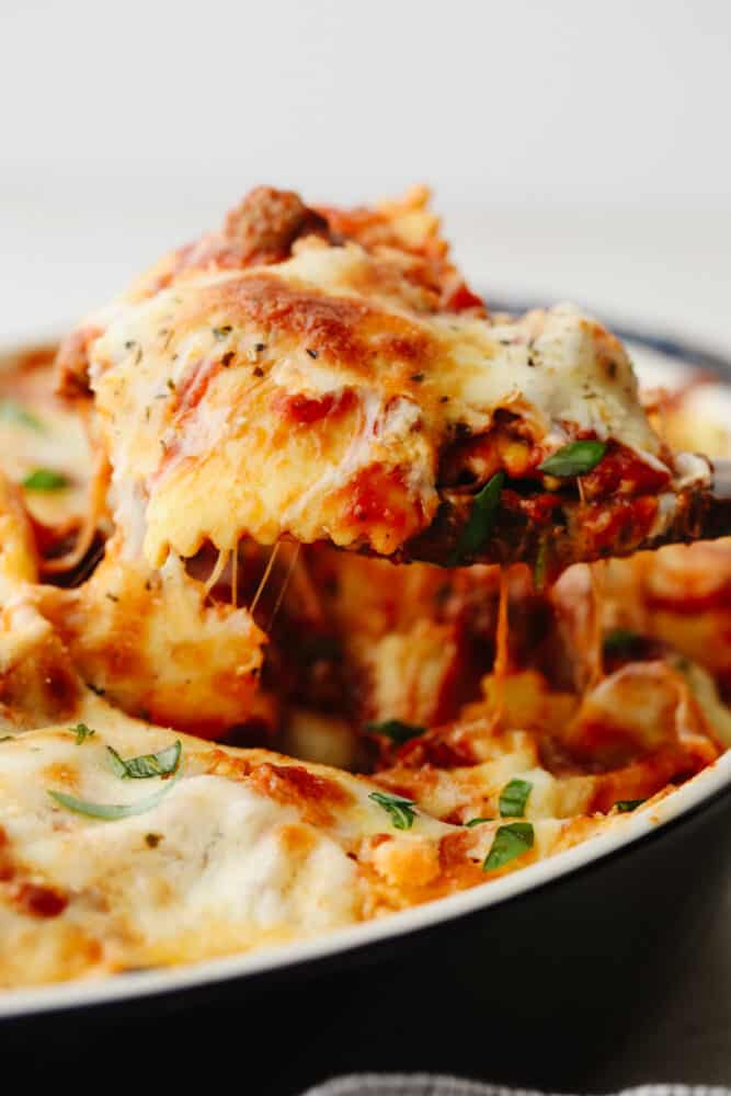 This baked ravioli is a knockout dinner that is sure to be loved by all! It's smothered in melty mozzarella, parmesan, and a tasty meat sauce! Scooping up ravioli with a wooden spoon.