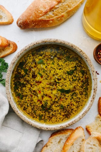This olive oil bread dip is the absolute perfect appetizer! It has just the right blend of spices that taste SOO GOOD! It will definitely get a "WOW!" from all of your guests! A bowl of olive oil dip with bread next to it.