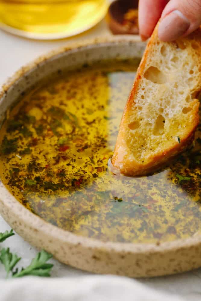 This olive oil bread dip is the absolute perfect appetizer! It has just the right blend of spices that taste SOO GOOD! It will definitely get a "WOW!" from all of your guests! A slice of bread being dipped into olive oil dip.
