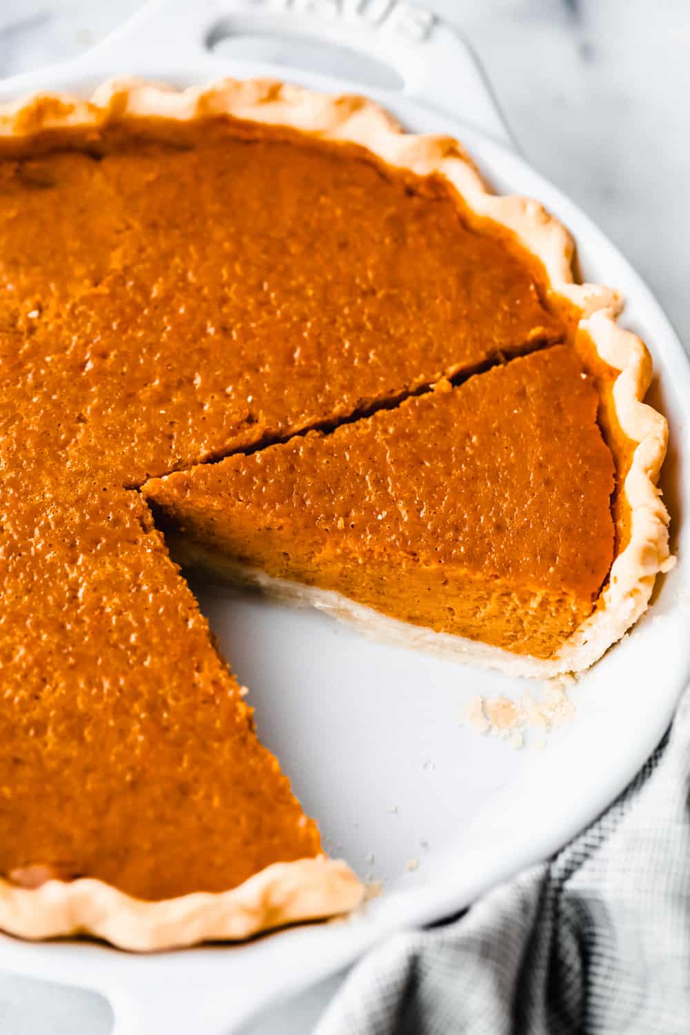 Grandma's famous pumpkin pie is smooth, thick, and creamy! A MUST for the holidays and the best when served with a big scoop of whipped cream on top! Pumpkin pie baked with a slice taken out of the pan.