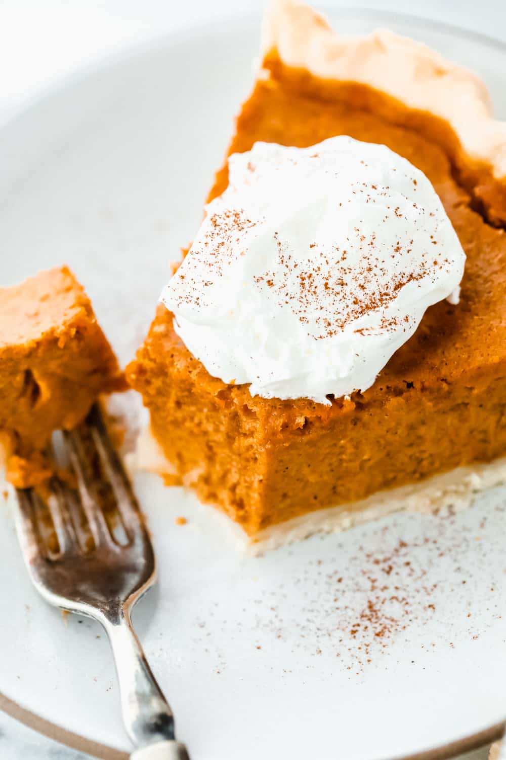 Grandma's famous pumpkin pie is smooth, thick, and creamy! A MUST for the holidays and the best when served with a big scoop of whipped cream on top! A sliced piece of pumpkin pie with a fork.