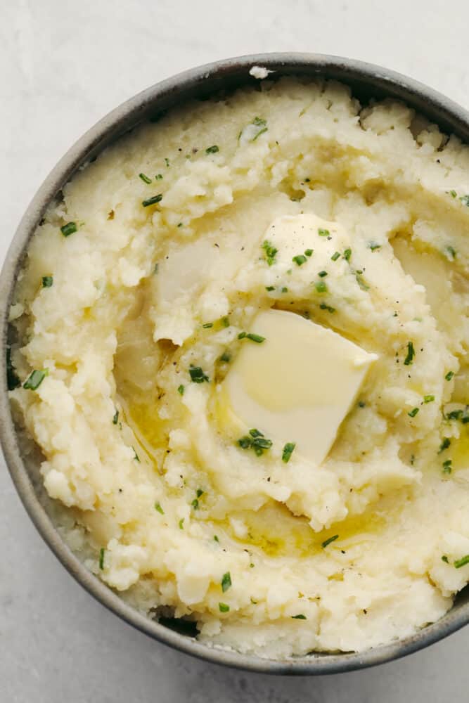 You MUST TRY these crockpot mashed potatoes! They are so creamy and delicous, plus they are super easy to make! Which makes them the perfect side for any meal. Mashed potatoes in a bowl with some butter and herbs on top.