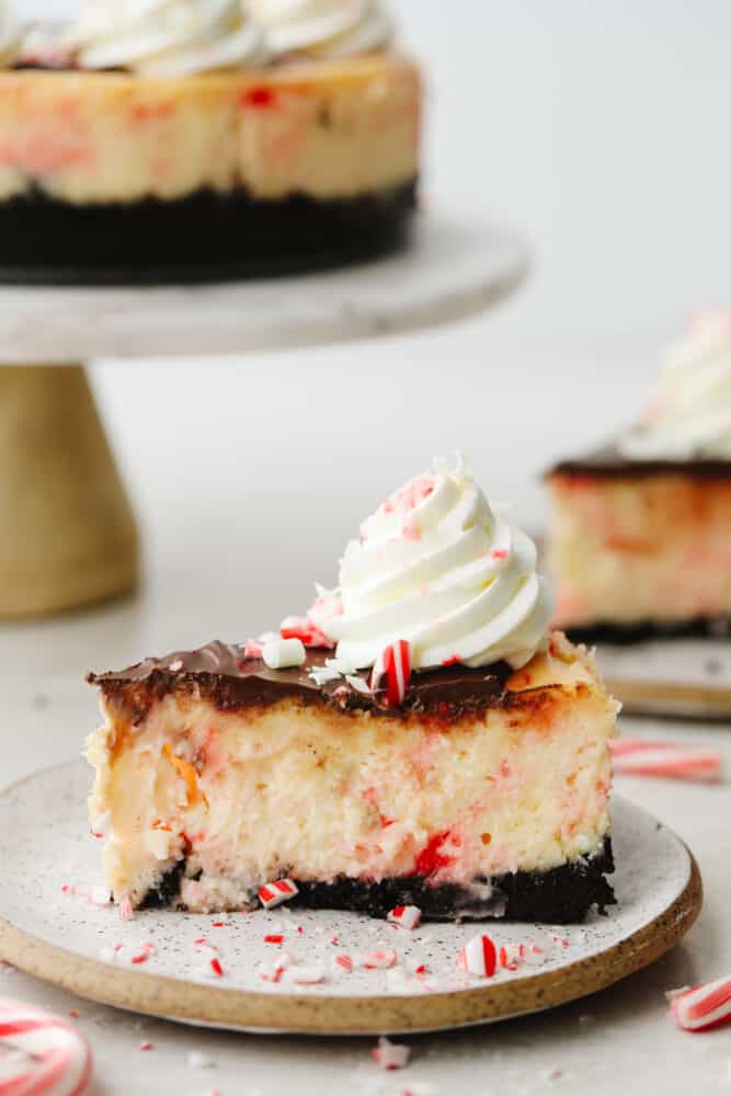 Peppermint cheesecake is creamy and delicious! It has the perfect oreo crust and is topped with crushed peppermint and whipped cream. This will definitely get a "WOW!" from all of your guests this holiday season! A slice of peppermint cheesecake on a plate.