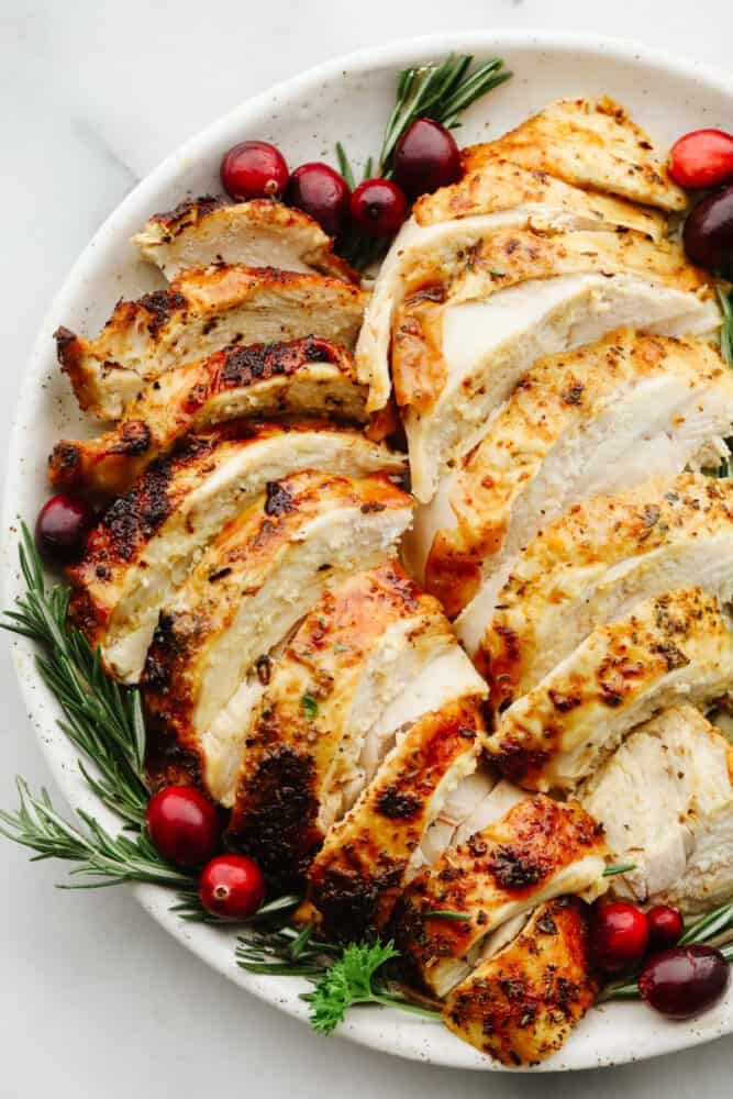 This juicy air fryer turkey is SOO GOOD and will have all of your guests asking for more! It's perfectly golden brown and dripping in flavor... You will never cook a turkey any other way again! Sliced turkey on a plate with garnish.
