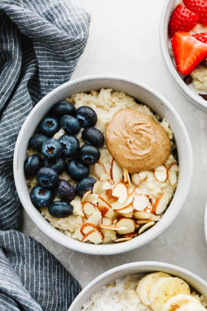 A warm, tasty bowl of homemade oatmeal is the perfect way to start your day! Here are 4 yummy variations filled with fresh fruit, nuts, brown sugar, and more! A bowl of oatmeal topped with almond slices, peanut butter, and blueberries.